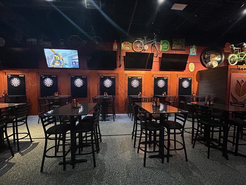 Seven numbered dartboard bays along the wall of the main game room, with high-top tables in front.
