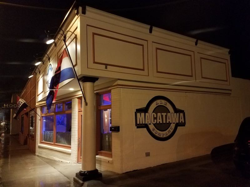 The Macatawa Ale Company building at night, its painted wall crest lit from the street.