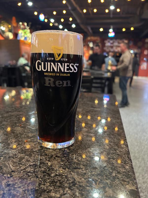 A pint of Guinness on the bar with the room lit up behind it.